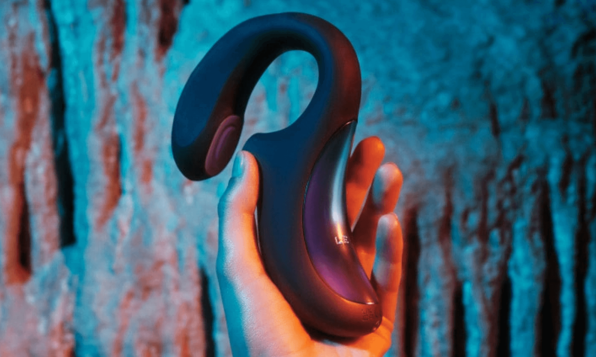 Woman holding black and purple vibrator in cave with teal lighting